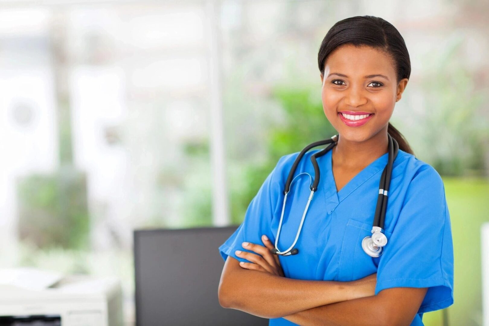 A woman in blue scrubs and stethoscope with her arms crossed.