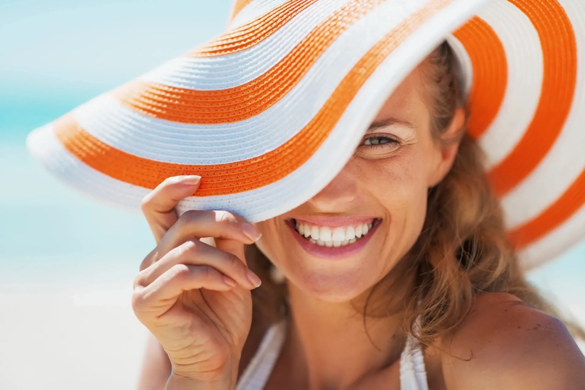 smiling woman under a sun hat with one eye hidden